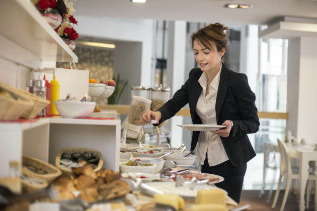 Adult businesswoman choosing food from a buffet table in a restaurant.